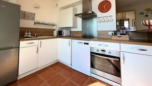 Una cuina moderna amb armaris blancs, una campana extractora d'acer inoxidable, un forn integrat, un microones i un rellotge de paret vermell.