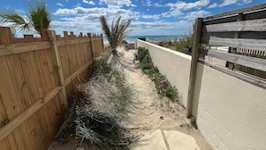 Una tanca de fusta, un camí de sorra i vista a la platja.