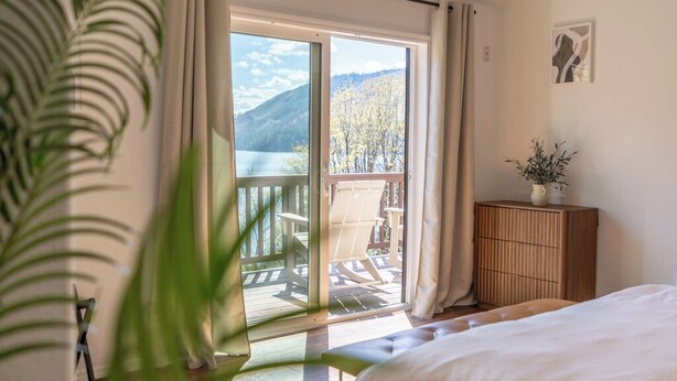 A bedroom with a bed, a wooden cabinet, a potted plant, and a balcony with a table and chairs.