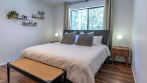 A bedroom with a large bed, bedside tables, a bench, and wall-mounted shelves with plants.