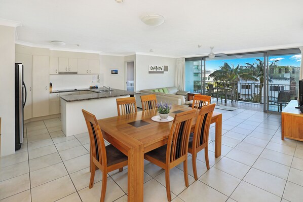 A modern kitchen with a dining area, large windows, and a view of palm trees.