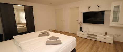 Et moderne hotelværelse med en stor seng, et fladskærms TV ophængt på væggen, trægulv og en mørk skænk.