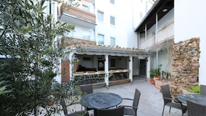 Un patio al aire libre con muebles de mimbre, una pared de piedra y vistas a un edificio con balcón.