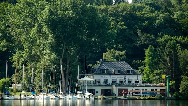 A lakeside building with a white facade and a dark roof, surrounded by dense trees. - Apartment in Essen with Balcony & Garden (Essen)