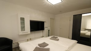 A hotel room with a bed, a TV mounted on the wall, a wardrobe, and a mirror. - Apartment in Essen with Balcony & Garden (Essen)
