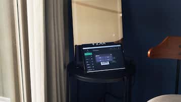 A tablet on a small table with a lamp, a wooden chair, and a curtain.