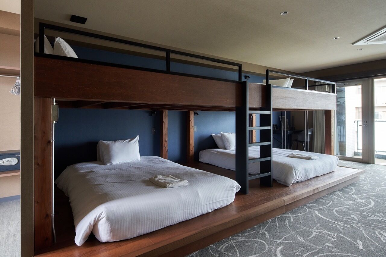 A hotel room with two bunk beds, a wooden headboard, and a large window offering a view.