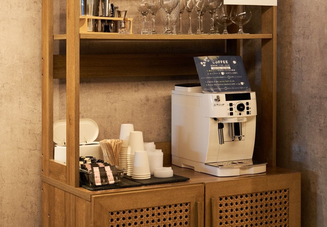 A coffee station with a coffee machine, disposable cups, and a sign indicating coffee service.