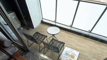 Uma varanda com uma mesa pequena e duas cadeiras, um purificador de ar Panasonic e uma parede revestida de azulejos.