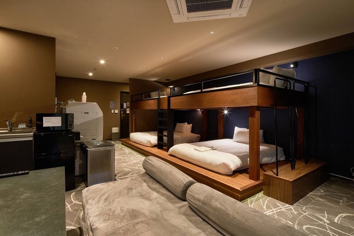 A hotel room with a bunk bed, a desk with a computer, a refrigerator, and a small kitchenette.