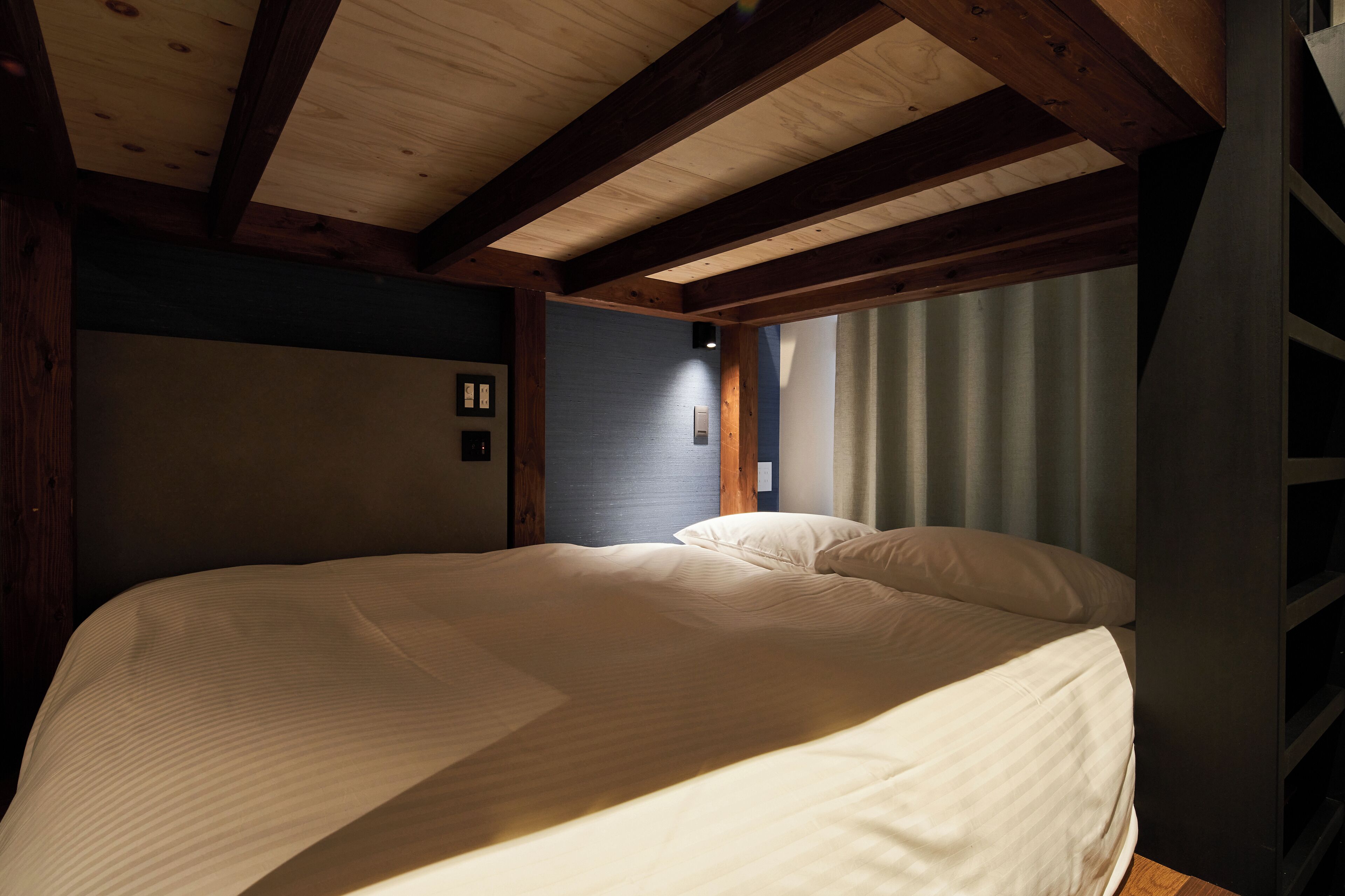 Une chambre avec un grand lit, des poutres en bois, une fenêtre avec des rideaux et un luminaire fixé au mur.
