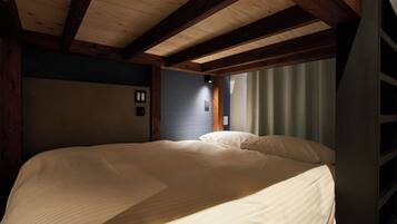 Une chambre avec un grand lit, des poutres en bois, une fenêtre avec des rideaux et un luminaire fixé au mur.