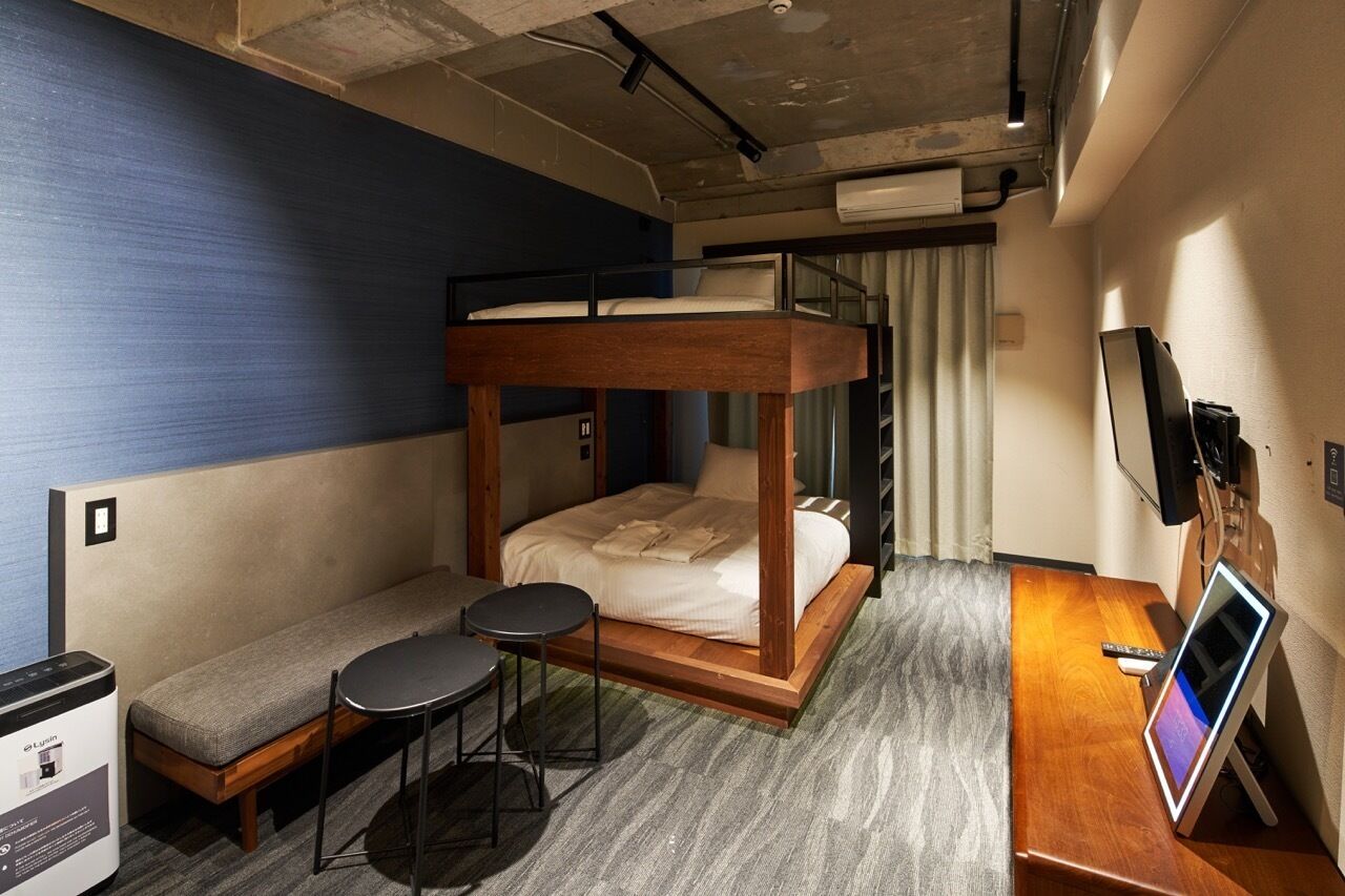 A bunk bed with a wooden frame, a small sofa, two round tables, a desk with a computer, and a TV.