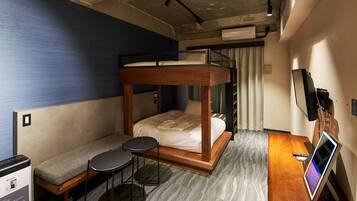 A bunk bed with a wooden frame, a small sofa, two round tables, a desk with a computer, and a TV.