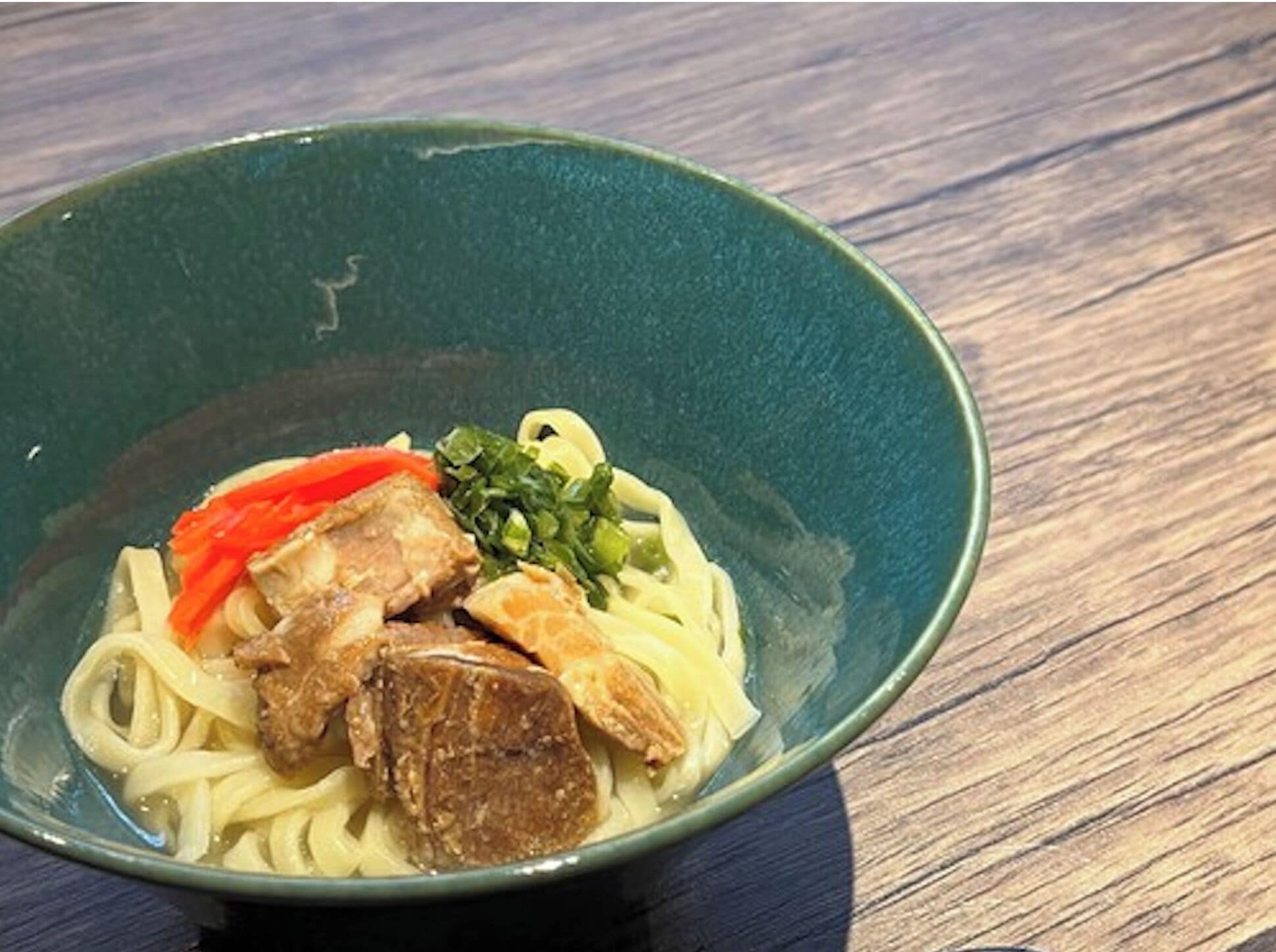 Eine Schüssel Ramen mit Nudeln, Fleisch und Gemüse auf einem Holztisch.