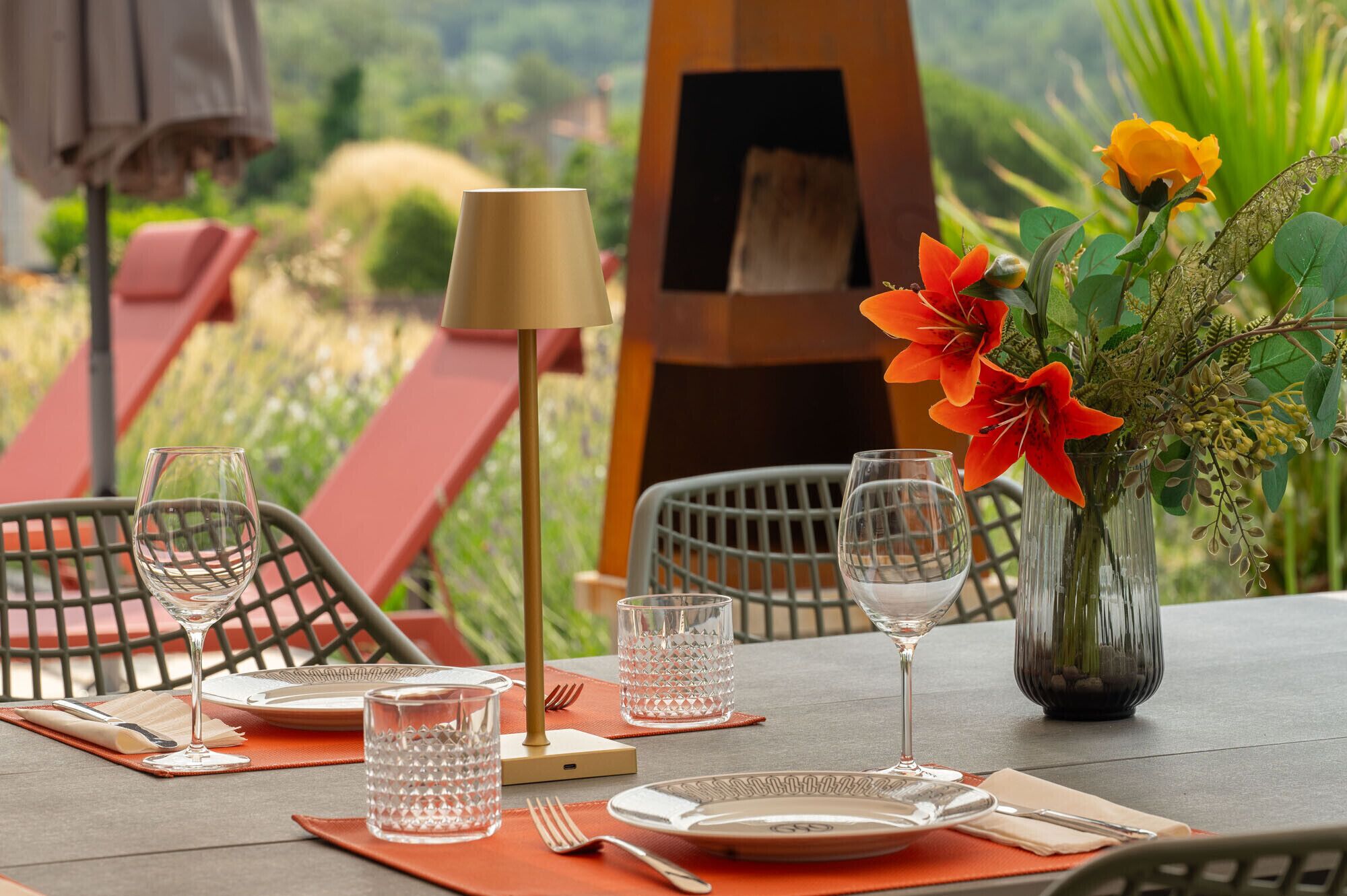 A dining table set with plates, glasses, cutlery, and a vase with flowers.