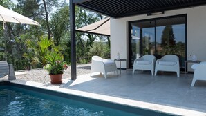 A modern outdoor pool area with a clear view of the surrounding trees, a covered seating area with white chairs, and a potted plant. - Villa Port des Vins – Luxury villa in Salernes with heated pool (Salernes)