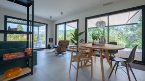 A modern living room with a round wooden table, two wooden chairs, a green sofa, and a bookshelf. - Villa Port des Vins – Luxury villa in Salernes with heated pool (Salernes)