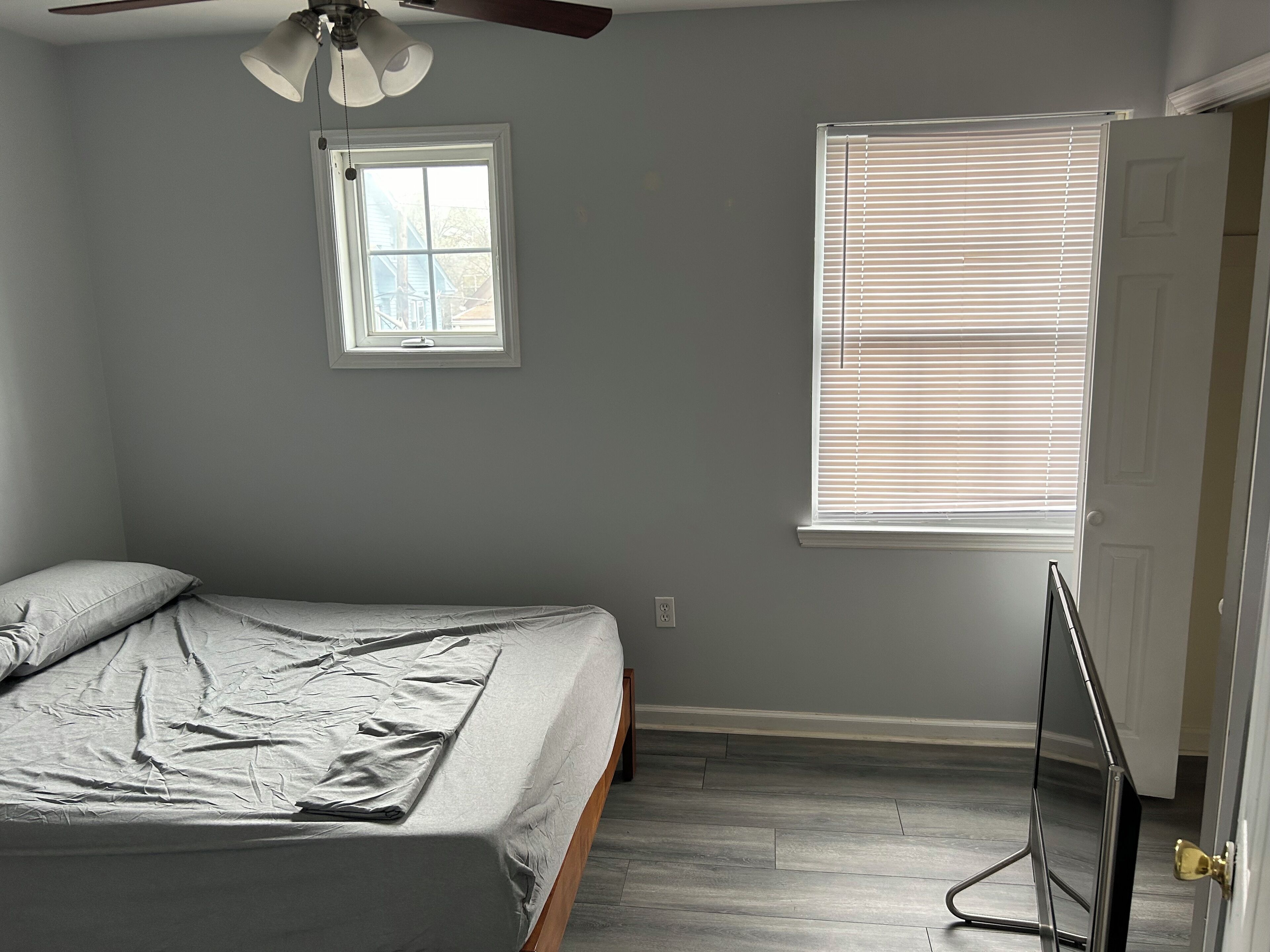 A bedroom with a bed, a ceiling fan, a window with blinds, and a door.