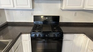 Una cocina con gabinetes blancos, estufa negra y encimera de granito.