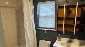 Un baño con bañera, inodoro y ventana con persianas.