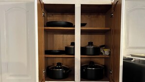 Un armario de cocina con dos ollas negras y una sartén en los estantes.