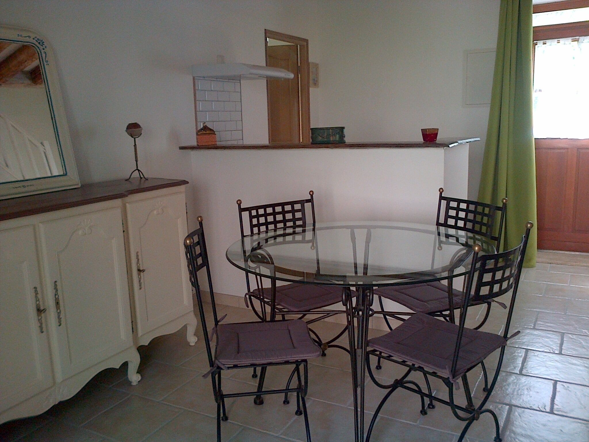 A dining area with a round glass table, four chairs, a white cabinet, and a mirror.