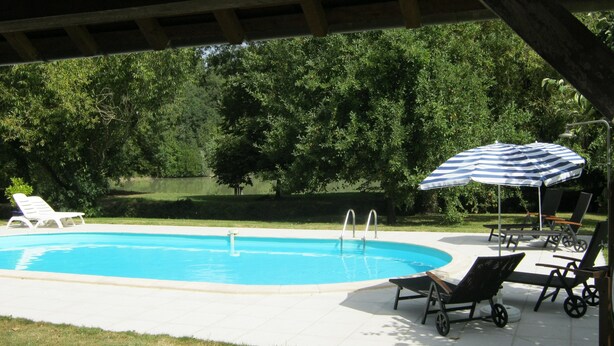 Ein Pool mit Liegestühlen und Sonnenschirm, umgeben von Bäumen.