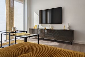 A modern living room with a glass coffee table, a sofa, a dark wood cabinet, and a flat-screen TV mounted on the wall. - Maisonette Ferienwohnung in Modernem Stil (Luckau)