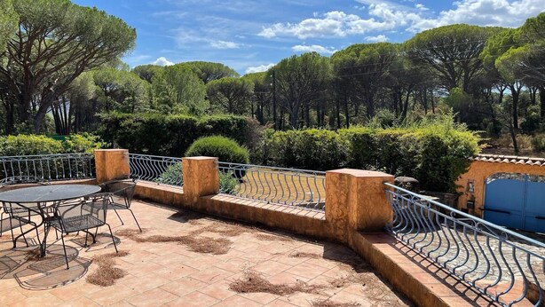 Eine Terrass mit rundem Tisch und Stühlen, umgeben von einem Metallgeländer und einer Steinmauer.