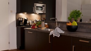Cocina moderna con armarios oscuros, un lavamanos de acero inoxidable, un microondas y una encimera con cafetera, tostadora y un cuenco de fruta.