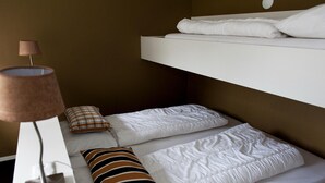 Una cama litera con ropa de cama blanca, una lámpara de noche y dos almohadas con estampados a rayas.