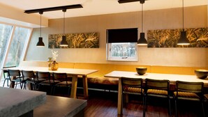 Interior de un restaurante con mesas altas, bancos e iluminación colgante.