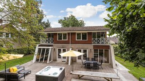 Una casa de dos pisos con un patio que cuenta con un jacuzzi, una mesa y mobiliario para exteriores.