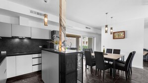 A modern kitchen with white cabinets, a black countertop, and a central island with a sink. There is a dining area with a wooden table and black chairs. - Villa in Istria with Heated Eco Pool (Brtonigla)