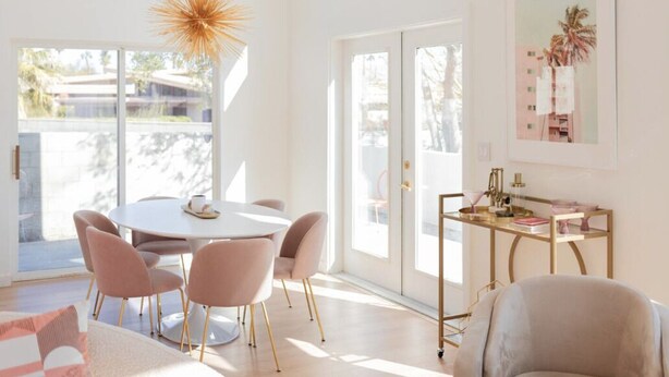 Une pièce lumineuse et ensoleillée, avec une table ronde, des chaises et un bureau à cadre doré, agrémenté d'un vase et de livres.