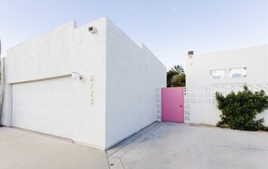 Een witte garage met een roze deur en het nummer '2723' op de muur.