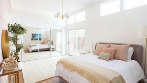Une chambre spacieuse avec un grand lit, un miroir et une plante en pot.