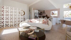 Un salon moderne avec un canapé blanc, une table basse en verre et une cuisine en arrière-plan.