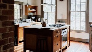 Une cuisine avec des meubles en bois, un îlot central, des luminaires suspendus et de grandes fenêtres.
