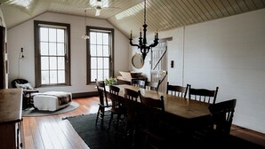 Un coin repas avec une table et des chaises en bois, de grandes fenêtres, un lustre et un miroir au mur.