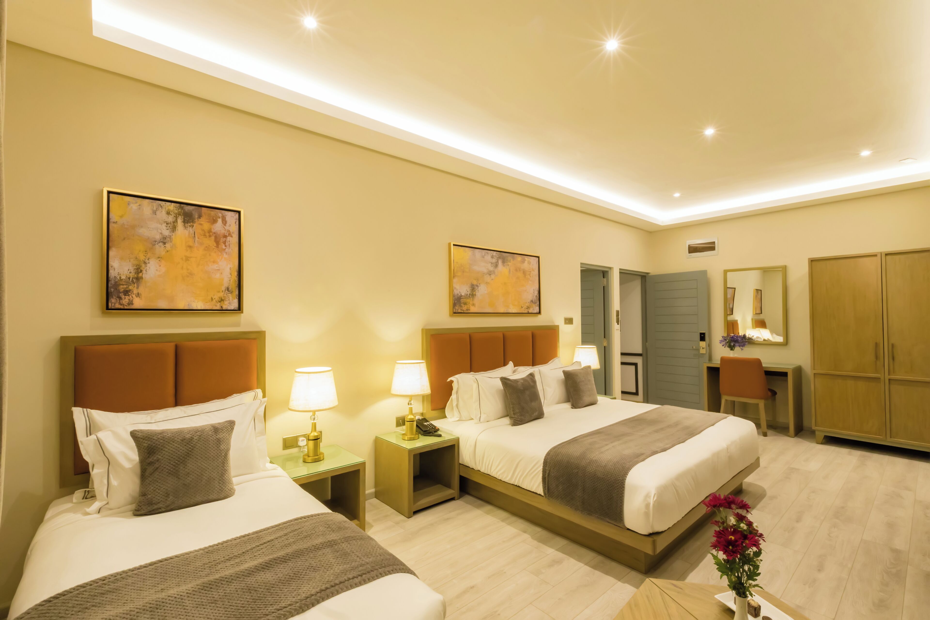 A hotel room with two beds, bedside tables with lamps, a desk, a chair, a mirror, and artwork on the walls.