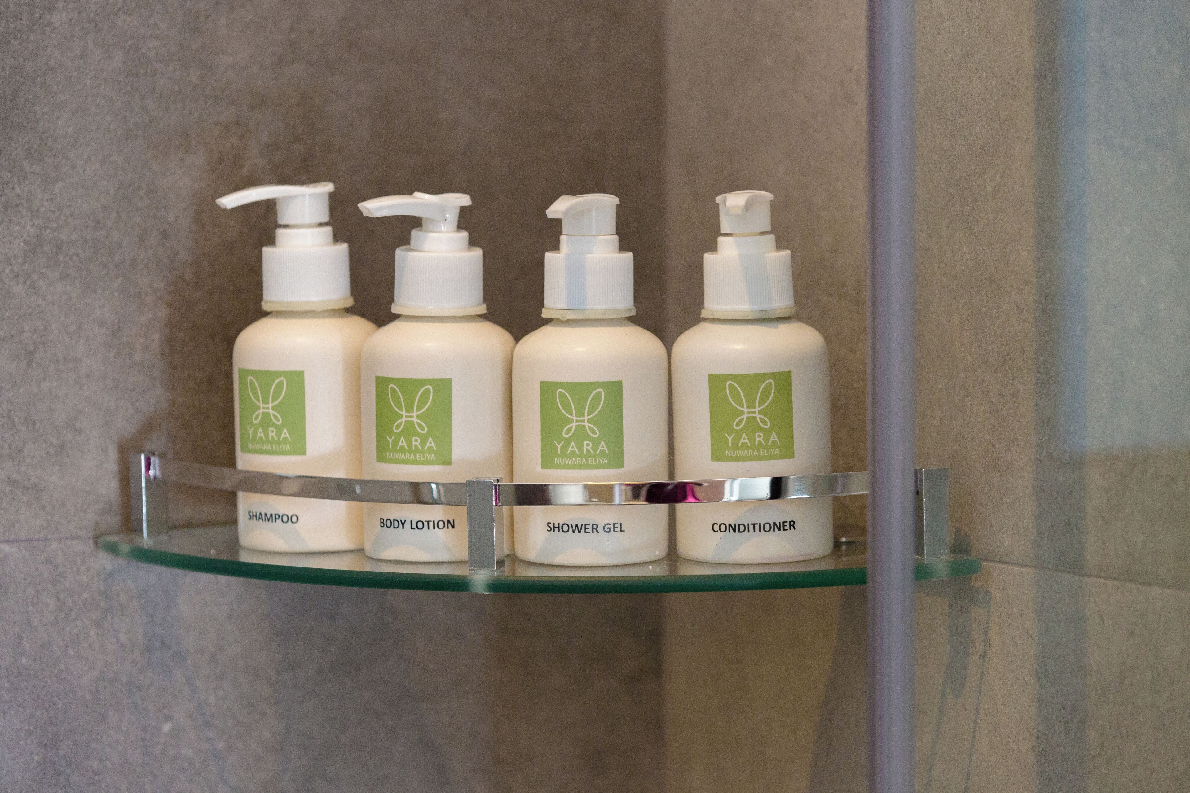 A bathroom shelf with four bottles of Yara Nuwara Eliva products: shampoo, body lotion, shower gel, and conditioner.