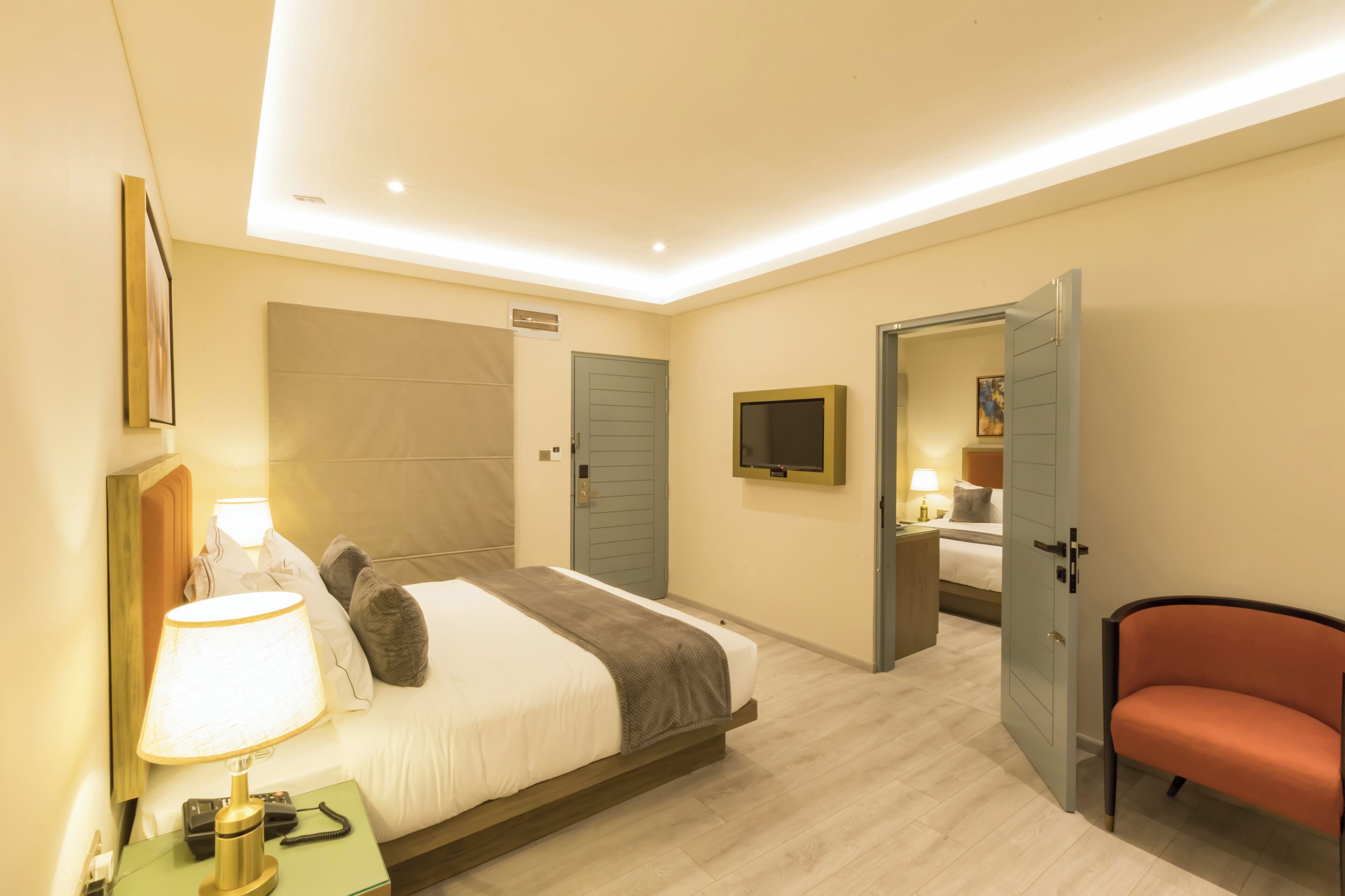 A hotel room with a bed, bedside table, lamp, TV, and a red chair.
