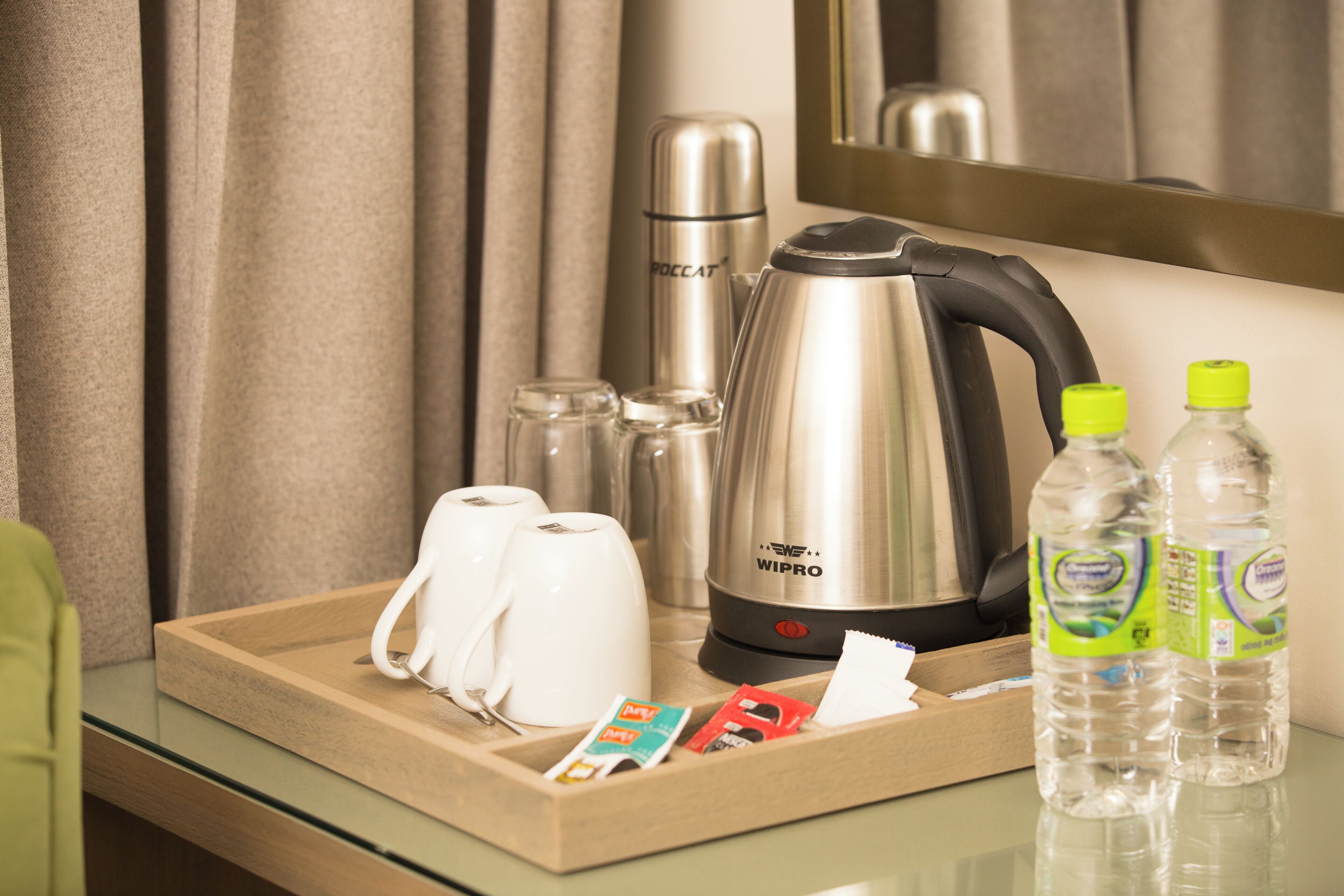 Ein Hotelzimmer mit Minibar, einem elektrischen Wasserkocher der Marke WIPRO, einer Kaffeemaschine, einem Tablett mit Toilettenartikeln und zwei Wasserflaschen.