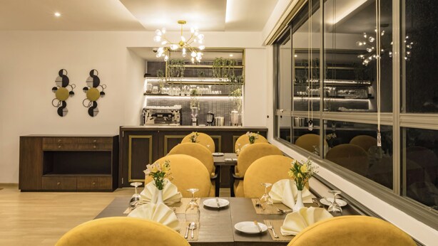 Un espace repas avec une longue table, des chaises jaunes et un lustre moderne.