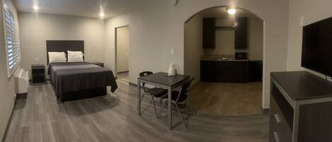 A hotel room with a bed, a desk, a chair, a TV, a microwave, and a small kitchenette.