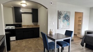 Une cuisine moderne avec des meubles de couleur sombre, un four à micro-ondes et une cuisinière. On y trouve un coin repas avec une table et des chaises, ainsi qu’un tableau accroché au mur.