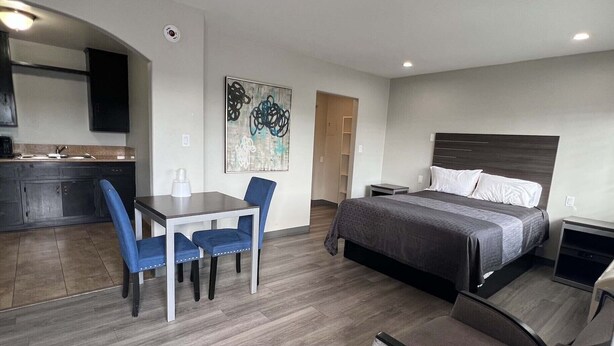 Une chambre d’hôtel moderne équipée d’un lit, d’un bureau avec des chaises, d’une kitchenette et d’un tableau au mur.