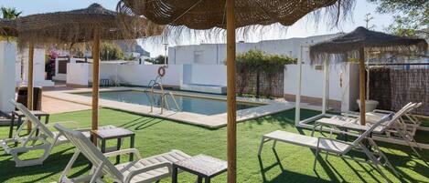 A pool area with white lounge chairs, a pool, and thatched umbrellas.